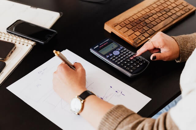 Services crop woman using calculator and taking notes on paper